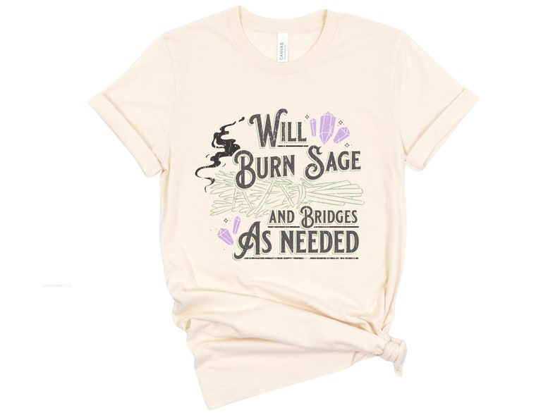 May include: A beige t-shirt with the text "Will Burn Sage and Bridges As Needed" printed on it. The text is in a black and white font with purple crystals and green sage bundles.