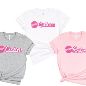 May include: Three t-shirts with the word "Custom" in pink lettering on a white, gray, and pink background.
