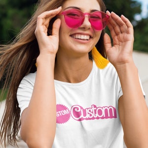 May include: A white t-shirt with a pink graphic that says "Custom" with a pink circle around the word "Custom" and the word "Stomp" inside the circle.