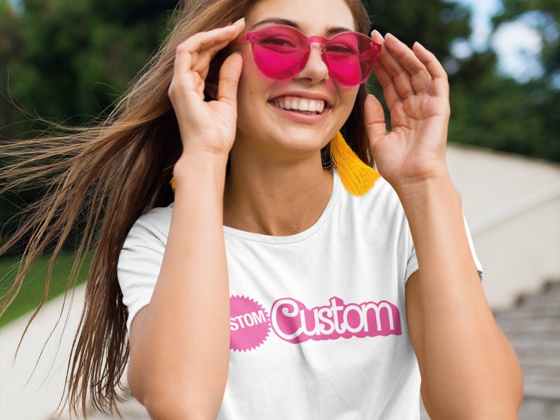 May include: A white t-shirt with a pink graphic that says "Custom" with a pink circle around the word "Custom" and the word "Stomp" inside the circle.