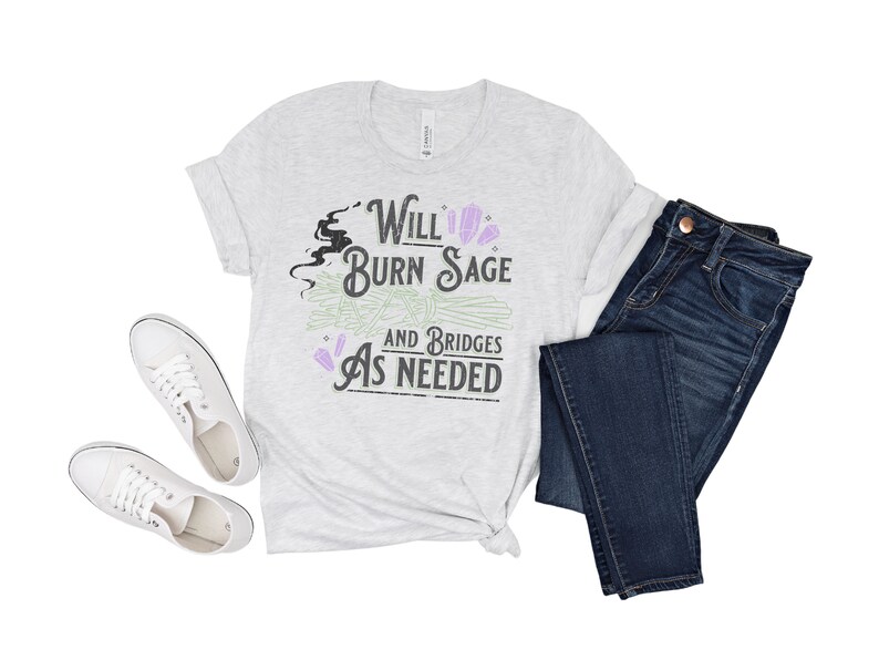 May include: A heather grey t-shirt with a graphic design that says "Will Burn Sage and Bridges As Needed". The graphic includes a black silhouette of a witch's head, a bundle of sage, and purple crystals.