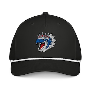 May include: A black baseball cap featuring a white rope detail across the base of the crown. The front displays an embroidered graphic of a blue dinosaur head wearing a red and silver crown, with sharp white teeth and a red tongue visible.