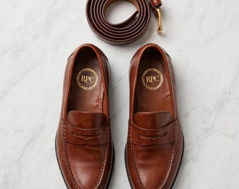 Handgemaakte bruine leren penny loafers met rode zool en bijpassende riem.