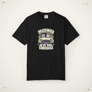 May include: A black short-sleeve t-shirt featuring a graphic of two cats in a car with the text "PASSENGER IN MY OWN CODEBASE". The illustration shows one cat driving with sunglasses and another cat looking surprised in the passenger seat.
