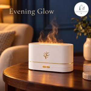 May include: A white, oval-shaped essential oil diffuser with a gold tree emblem on the front, emitting a warm, orange-toned mist. The device features horizontal ribbed detailing at the base, two gold buttons, and the text Evening Glow.