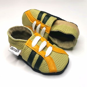 Puede incluir: Zapatos de bebé verde oliva con detalles en naranja y negro. Los zapatos tienen cordones blancos y la palabra "EBOOBA" en una etiqueta. Están hechos de cuero perforado y tienen un interior suave.