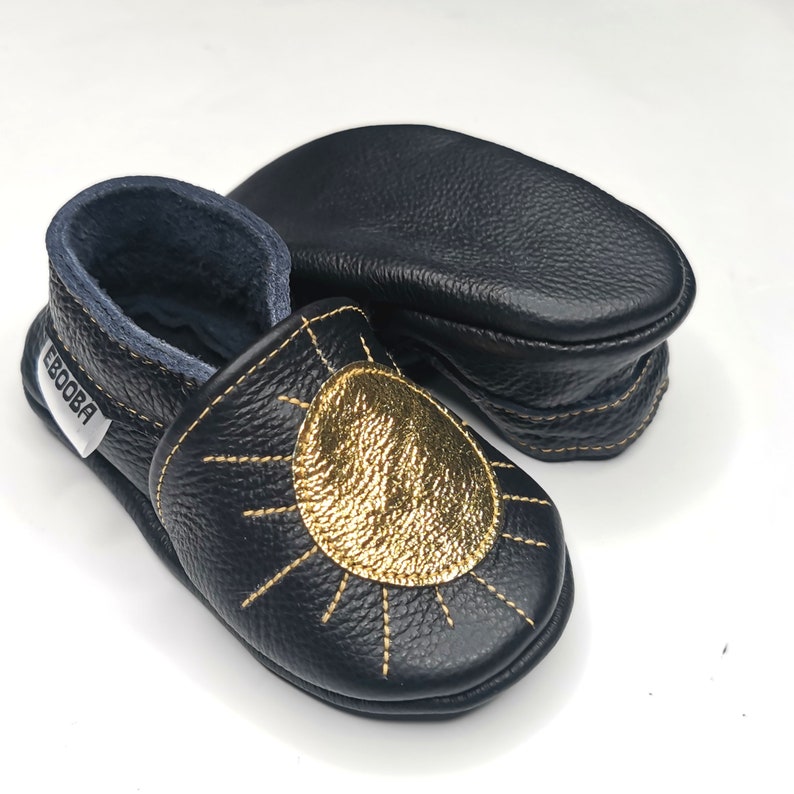 May include: Black leather baby shoes with a gold sun design and the word "Ebooba" on the side.