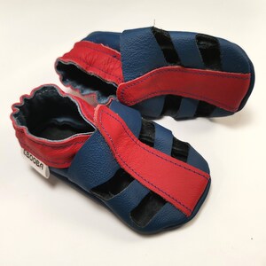 May include: A pair of blue and red leather baby sandals with a strap across the top and a small label that says "Ebooba".