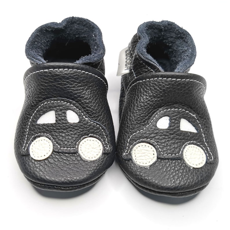 May include: Black leather baby shoes with a white car design. The shoes have a soft, flexible sole and are perfect for crawling and walking.
