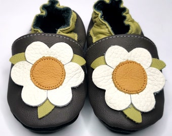 Può includere: Un paio di scarpine per neonati in pelle marrone con un design a margherita bianca. I fiori hanno un centro giallo e foglie verdi.