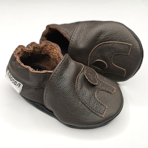 K&ouml;nnte beinhalten: Ein Paar braune Lederschuhe f&uuml;r Babys mit einem gestickten Elefantenmuster. Die Schuhe haben eine weiche, flexible Sohle und eine bequeme Passform.