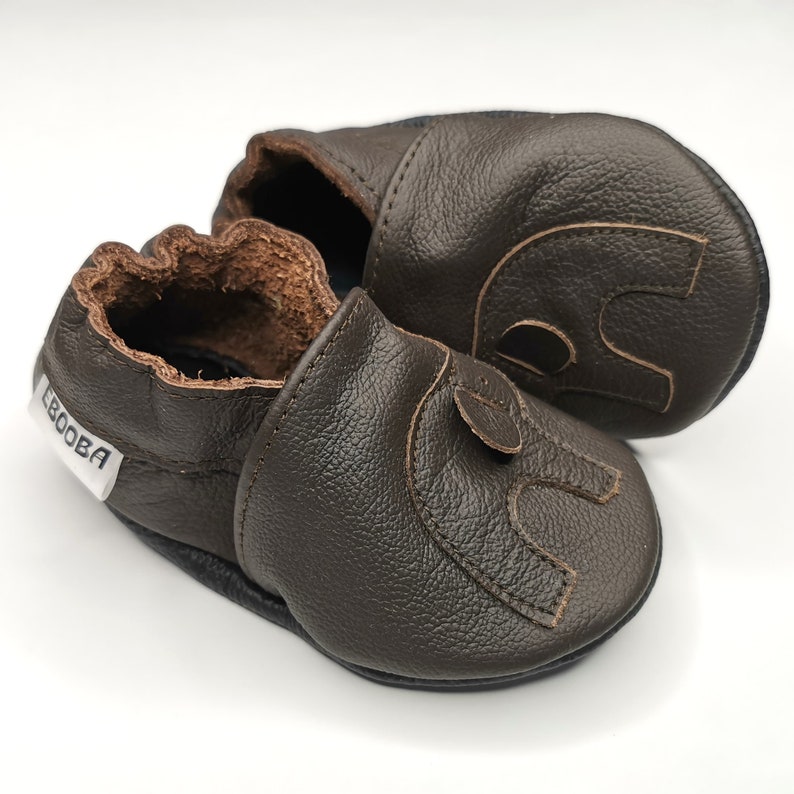 K&ouml;nnte beinhalten: Ein Paar braune Lederschuhe f&uuml;r Babys mit einem gestickten Elefantenmuster. Die Schuhe haben eine weiche, flexible Sohle und eine bequeme Passform.
