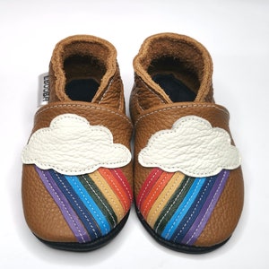 May include: A pair of brown leather baby shoes with a white cloud and rainbow design. The shoes have a black sole and are made of soft leather.