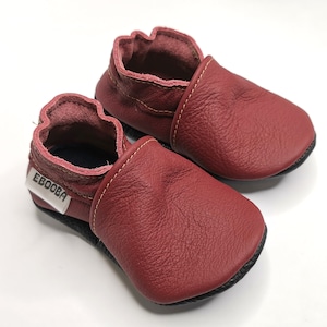 May include: A pair of burgundy leather baby shoes with a black sole and a white label that says "Ebooba".
