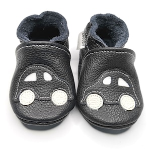 May include: Black leather baby shoes with a white car design. The shoes have a soft, flexible sole and are perfect for first steps.