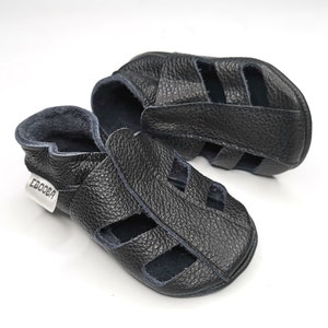 May include: A pair of black leather sandals with a strap across the top and an open toe design. The sandals have a blue lining and the brand name "Ebooba" is printed on the side.
