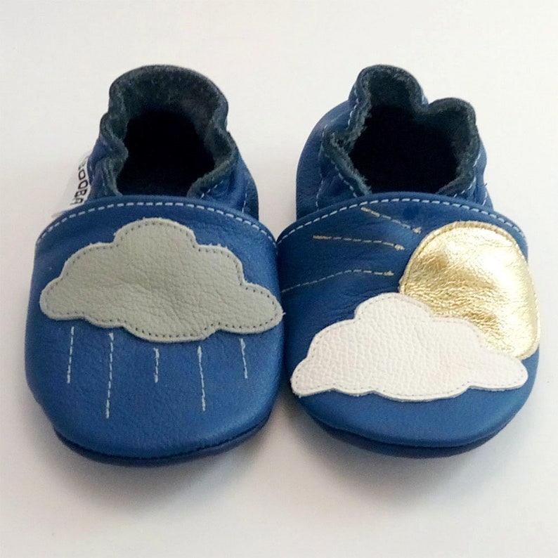 May include: A pair of blue leather baby shoes with a cloud and raindrop design on one shoe and a cloud and sun design on the other shoe.