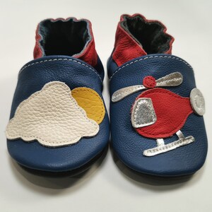 Peut inclure: Une paire de chaussures de bébé en cuir bleu avec un motif nuage et soleil sur une chaussure et un motif d'hélicoptère rouge sur l'autre.