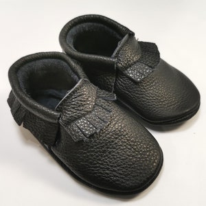 May include: A pair of black leather baby moccasins with fringe detail.