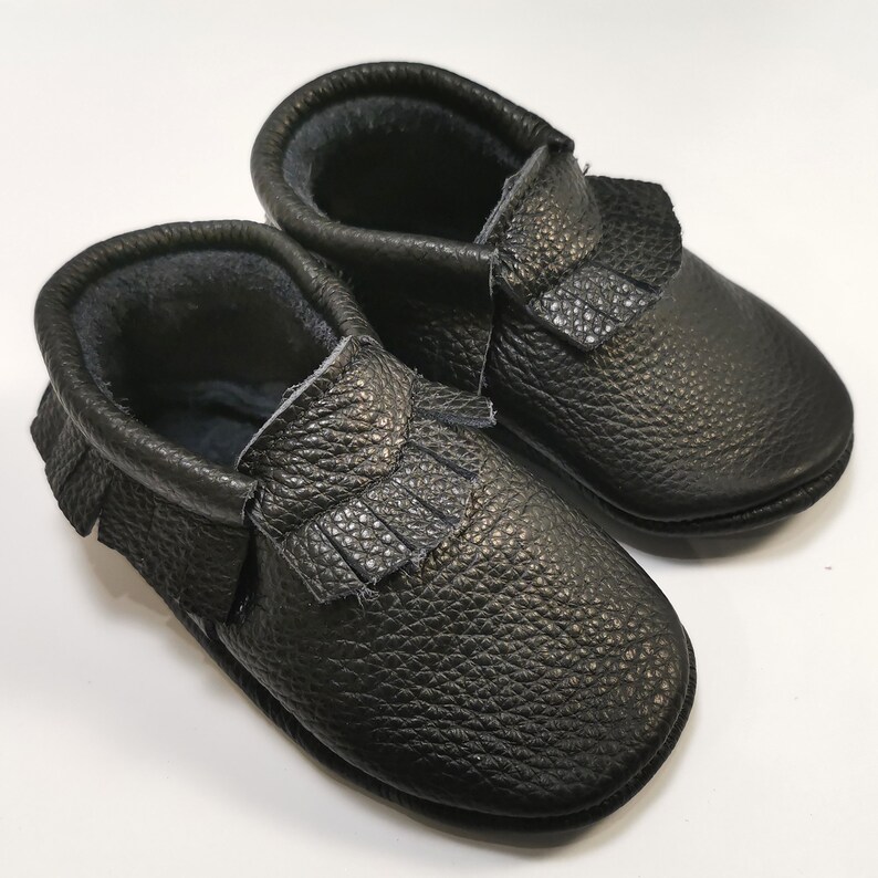 May include: A pair of black leather baby moccasins with fringe detail.