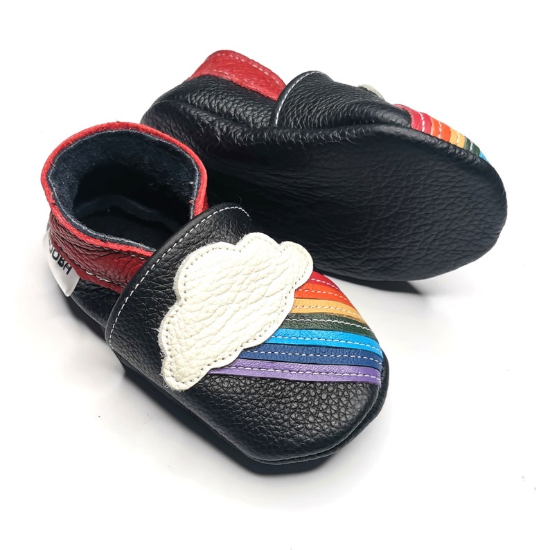 May include: Black leather baby shoes with a rainbow and cloud design. The shoes have a red trim and a white cloud with a rainbow around it.