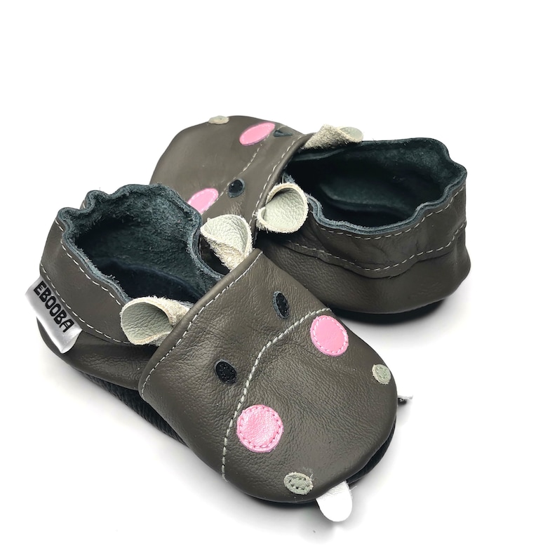 May include: A pair of brown leather baby shoes with a hippopotamus design. The shoes have pink and green accents and the text "Ebooba" is printed on the side.