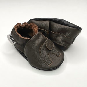 K&ouml;nnte beinhalten: Ein Paar dunkelgr&uuml;ne Lederschuhe f&uuml;r Babys mit einem braunen Lederriemen und einem wei&szlig;en Etikett mit der Aufschrift "Ebooba".