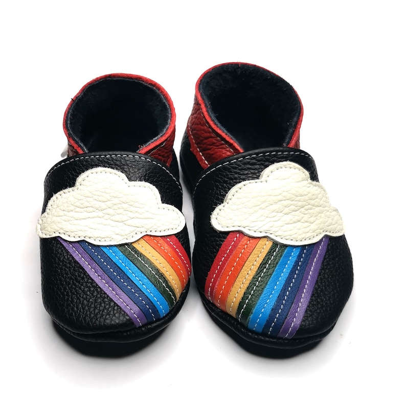 May include: Black leather baby shoes with a rainbow and cloud design. The shoes have a white cloud with a rainbow coming out of it.