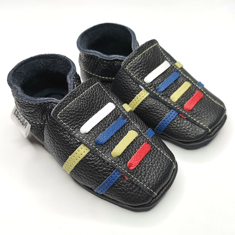 May include: A pair of black leather baby shoes with colorful stripes. The shoes have a label that says "Ebooba".