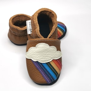 May include: A pair of brown leather baby shoes with a rainbow and cloud design. The shoes have a white cloud with a rainbow underneath it.
