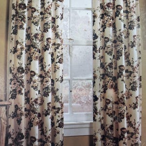 May include: A pair of floor-length curtains featuring a cream background with a dense floral pattern in shades of brown, dark green, and muted rose. The curtains are hung on a rod with tab tops and display a pleated header design.