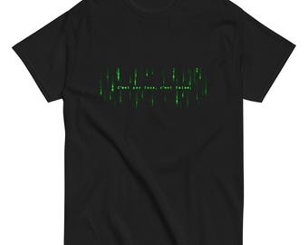 May include: A black short-sleeved t-shirt featuring a central graphic of vertical green digital rain patterns. The text C'est pas faux, c'est false; is printed in a white monospaced font across the centre of the green digital design.