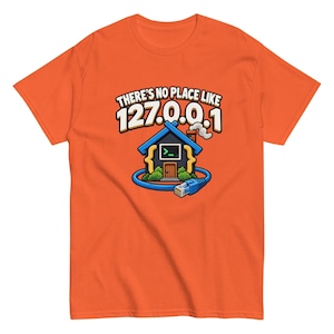 Może przedstawiać: Pomarańczowy t-shirt z krótkim rękawem z grafiką przedstawiającą dom z kominem i owiniętym wokół niego niebieskim kablem ethernetowym. Tekst nad domem brzmi "THERE'S NO PLACE LIKE 127.0.0.1", a wewnątrz domu widać symbol terminala komputerowego.