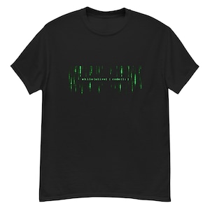 Może przedstawiać: Czarny t-shirt z krótkim rękawem z nadrukiem graficznym przedstawiającym zielony, pionowy cyfrowy deszcz kodu. Na środku wzoru znajduje się biały napis while(alive) { code(); }.