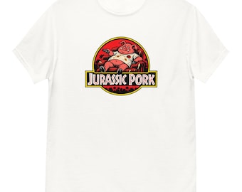 May include: A white short-sleeved t-shirt featuring a graphic of a pig sitting in a red armchair holding a remote control. The circular design includes the text JURASSIC PORK in white letters with a black outline on a yellow and black rectangular banner.