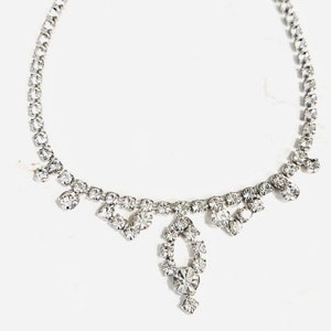 May include: A silver necklace with a delicate chain and a dangling crystal pendant. The pendant is made up of smaller crystals arranged in a teardrop shape.