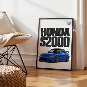 May include: A framed vertical poster featuring a blue Honda S2000 sports car illustration. The text HONDA S2000 is printed in large black capital letters above the car, with a small Honda logo emblem positioned in the top right corner.