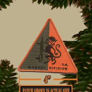 May include: A 4-inch triangular patch with a green and orange background. A black monkey holding a rifle is in the center of the patch. The text "Monkey Division T.M." is printed on the patch.