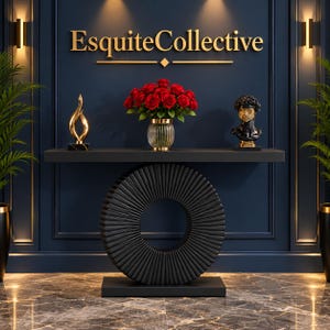 May include: A black console table with a large circular, ribbed base. On the table sits a glass vase filled with red roses, a gold flame-shaped sculpture on a black base, and a black and gold bust. The text EsquiteCollective is on the wall.