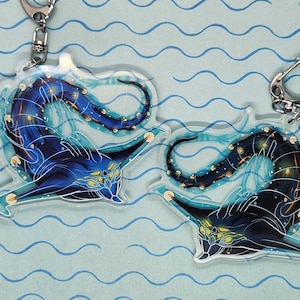 May include: Two blue and black creature keychains with gold accents. The creatures are stylized and have a bioluminescent quality. The keychains are hanging from silver chains.