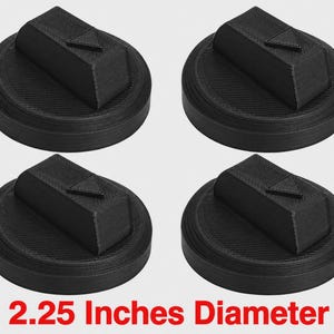 Peut inclure: Un ensemble de quatre boutons de commande de cuisinière noirs circulaires, chacun doté d'une poignée rectangulaire surélevée avec un petit indicateur triangulaire pointant vers le haut. Les boutons ont une surface texturée et mesurent 5,715 cm de diamètre.