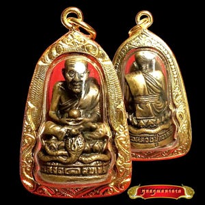 May include: Two bronze-colored amulets featuring a seated monk figure with a cobra at the base, encased in ornate gold-toned metal frames with red accents. The front shows the monk holding a sphere, while the back shows the monk from behind.