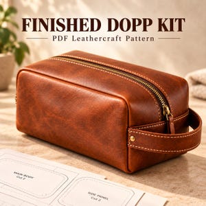 May include: A brown leather dopp kit with a brass zipper and a side handle, featuring visible stitching. The text FINISHED DOPP KIT PDF Leathercraft Pattern is displayed above. A paper pattern with labels MAIN BODY and SIDE PANEL is visible below.