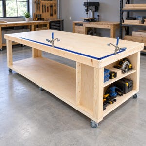 May include: A large, rectangular light-colored wooden workbench on wheels featuring a blue metal track system with two adjustable clamps mounted on top. The base includes an open storage shelf holding various power tools and cases.
