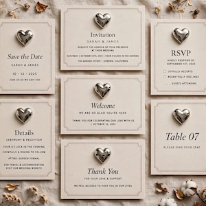 Könnte beinhalten: Ein Set aus sechs cremefarbenen Hochzeitspapeterie-Karten mit schwarzem Serifentext und einer mittigen, silbernen herzförmigen Verzierung auf jeder Karte. Die Karten umfassen Save the Date, Invitation, RSVP, Welcome, Details, Table 07 und Thank You.