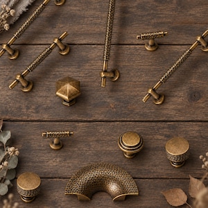 May include: A collection of antique brass cabinet hardware featuring various shapes including long bar pulls, T-bar handles, round knobs, and a semi-circular pull. Each piece displays a textured, hammered finish with a dark, weathered patina.