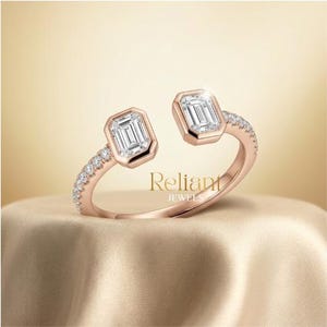 Könnte beinhalten: Ein offener Ring aus Roségold mit zwei Diamanten im Smaragdschliff an den Enden, akzentuiert durch kleine runde Pavé-Diamanten entlang der Ringschiene. Der Text Reliant JEWELS steht mittig im offenen Bereich.