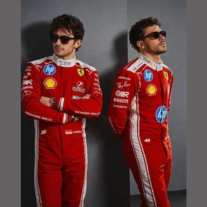 May include: Two individuals wearing red racing suits with white side stripes and various sponsor logos including HP, Shell, and IBM. Both wear dark sunglasses and stand against a grey background. One suit features the number 16 and the other 44.