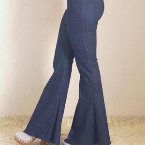 May include: Dark blue denim flare pants. The pants have a high waist and a wide bell bottom. The model is wearing white clogs with a wooden heel. The pants are on a white fluffy rug.