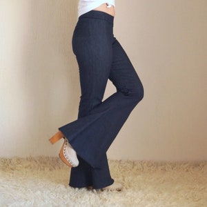 May include: Dark blue flared pants with a high waist. The pants are paired with white clogs with a wooden heel. The outfit is set against a neutral background and a white rug.